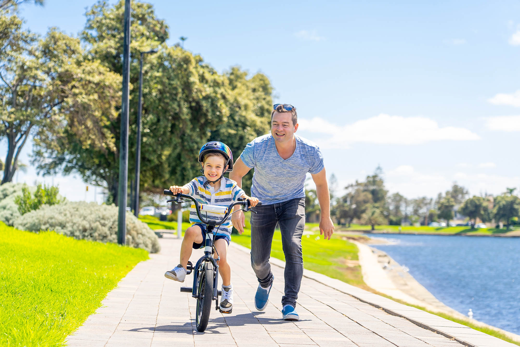 Father helping son ride a bicyle, on a path next to a river