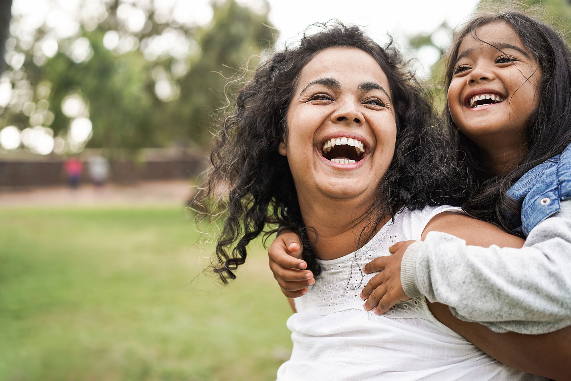 Mother carrying child on her back, both laughing and smiling