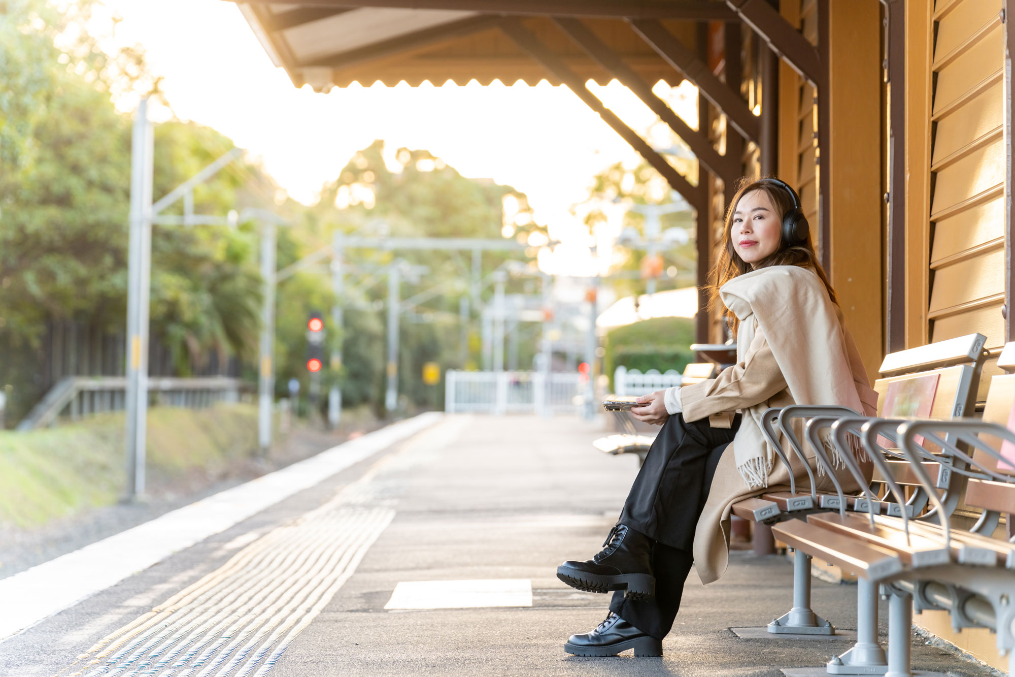 Young lady sitting on a train station bench wearing headphones