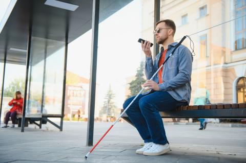 A blind person with a walking stick sitting at a bus stop